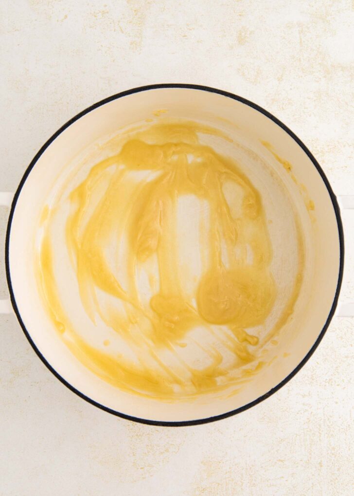A white pot with a thin layer of melted butter spread across the bottom, sitting on a light-colored surface.