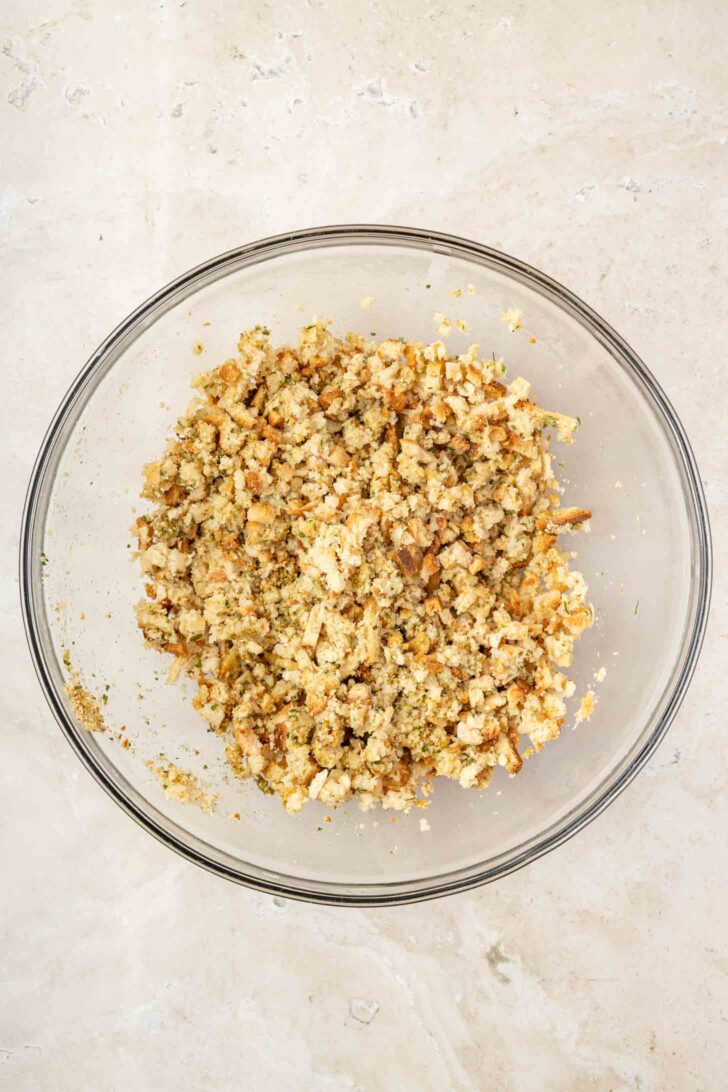 A clear glass bowl filled with seasoned bread stuffing mix sits on a light-colored countertop.