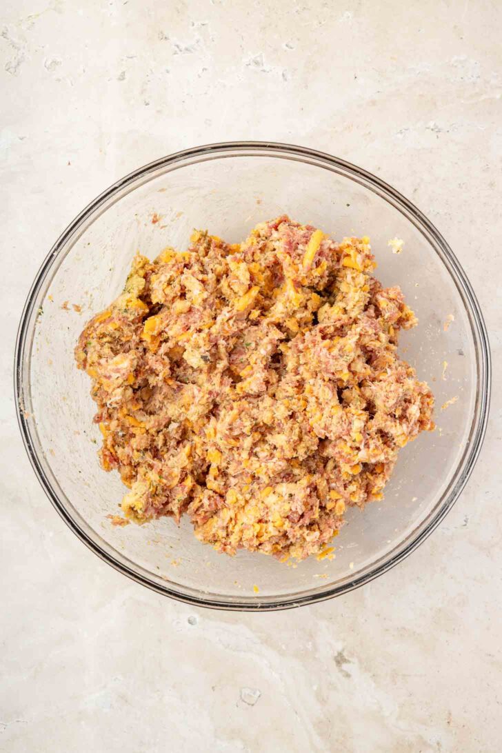 A glass bowl filled with a mixed ground meat and breadcrumb mixture sits on a light-colored countertop.