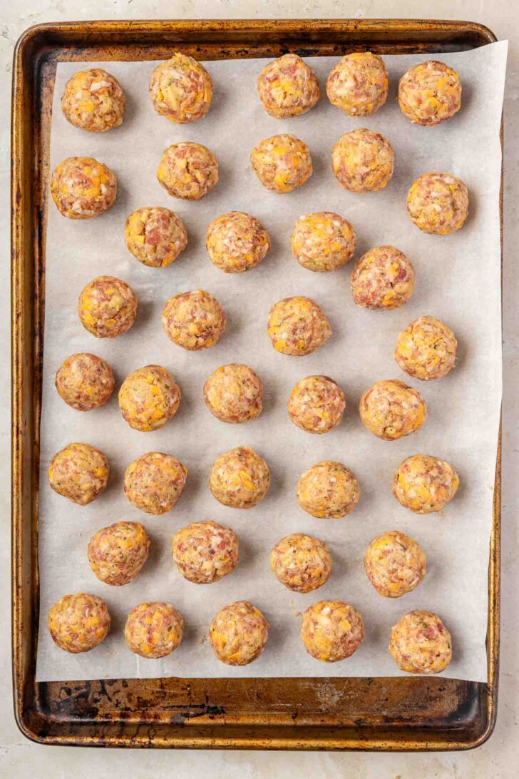 Thirty-six uncooked sausage balls arranged in neat rows on a parchment-lined baking sheet, ready to be baked.